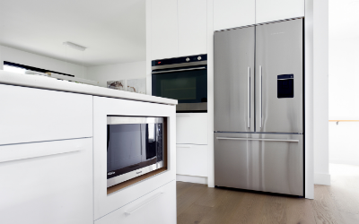 stainless steel microwave built into white cabinets and a large fridge and wall unit oven in the background | does a kitchen renovation increase the value of my home?
