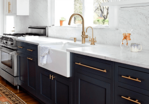 Blue cabinets with gold coloured handles and a gold tap with white and grey marble counter top