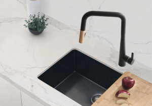 Matte black and gold faucet with over a black sink and white marble counter top showing two toned faucet. Apple on a cutting board.