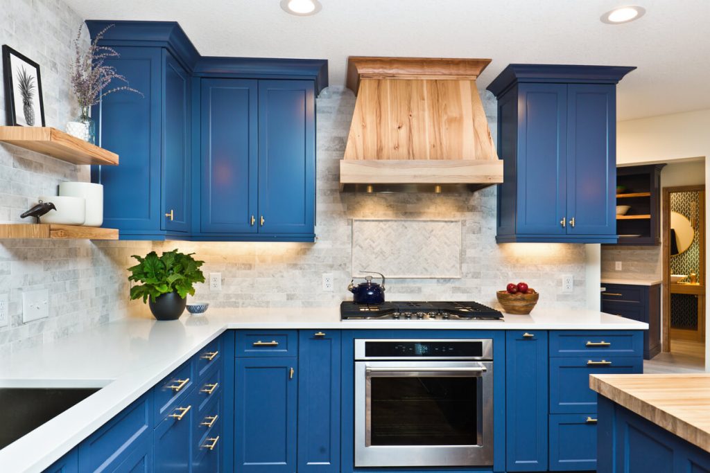 Blue cabinets in a kitchen with stone backsplash and a light wood grain hood vent