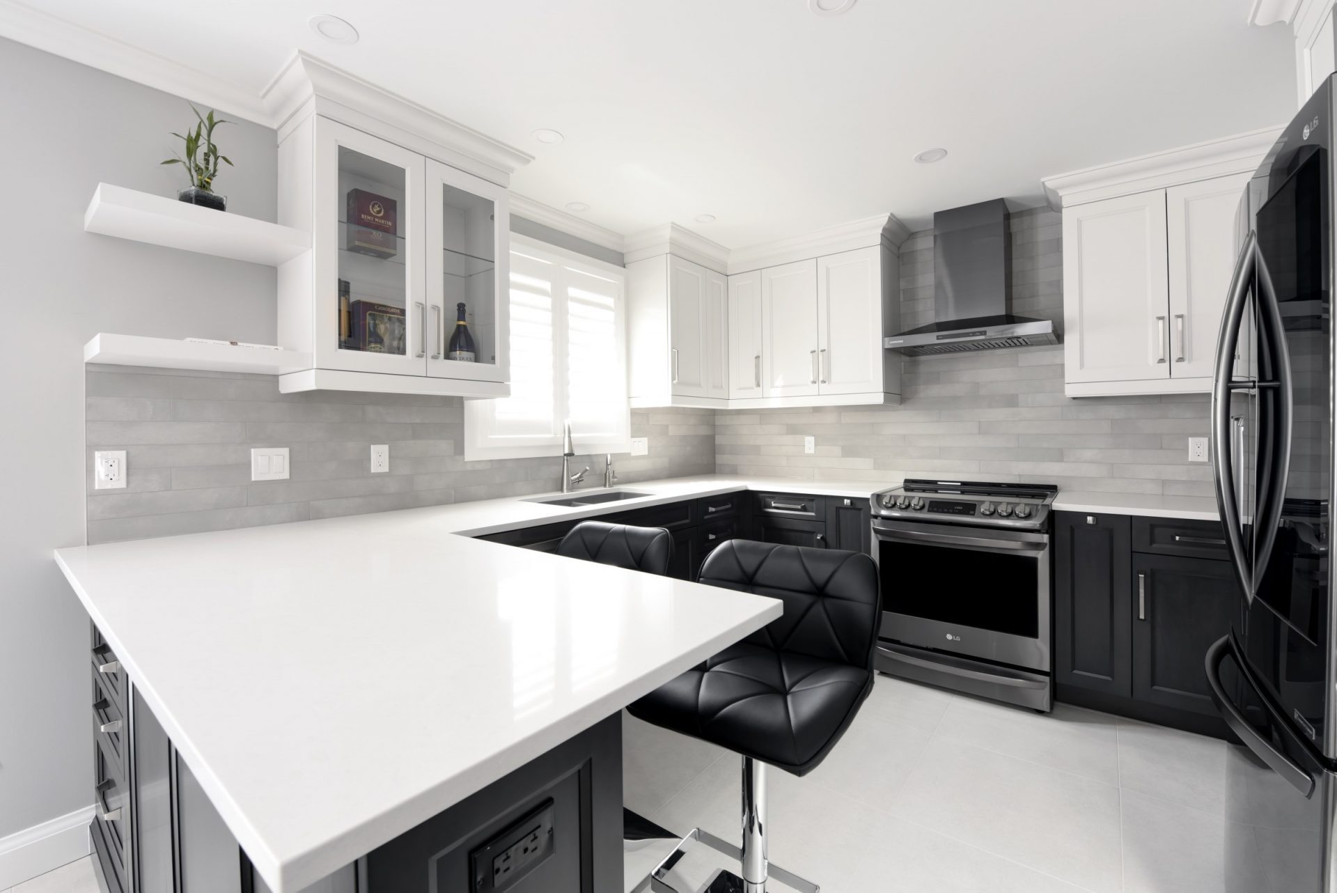 Stylish two-tone kitchen with black lower cabinets, white uppers, light gray tile backsplash, quartz countertops, and modern stainless steel appliances.