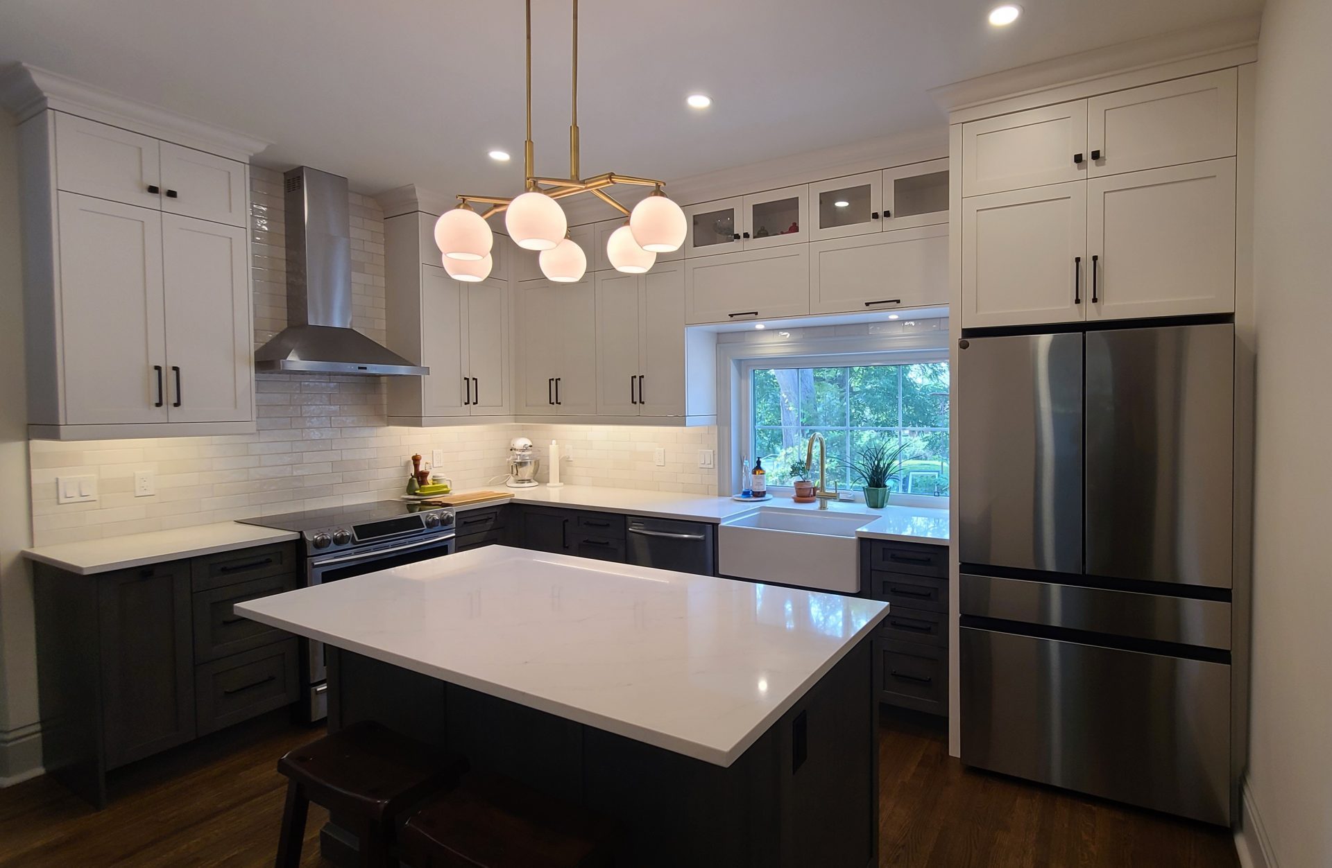 Elegant modern kitchen with two-tone cabinetry, white quartz island, stainless steel appliances, farmhouse sink, and a gold chandelier with globe lights.