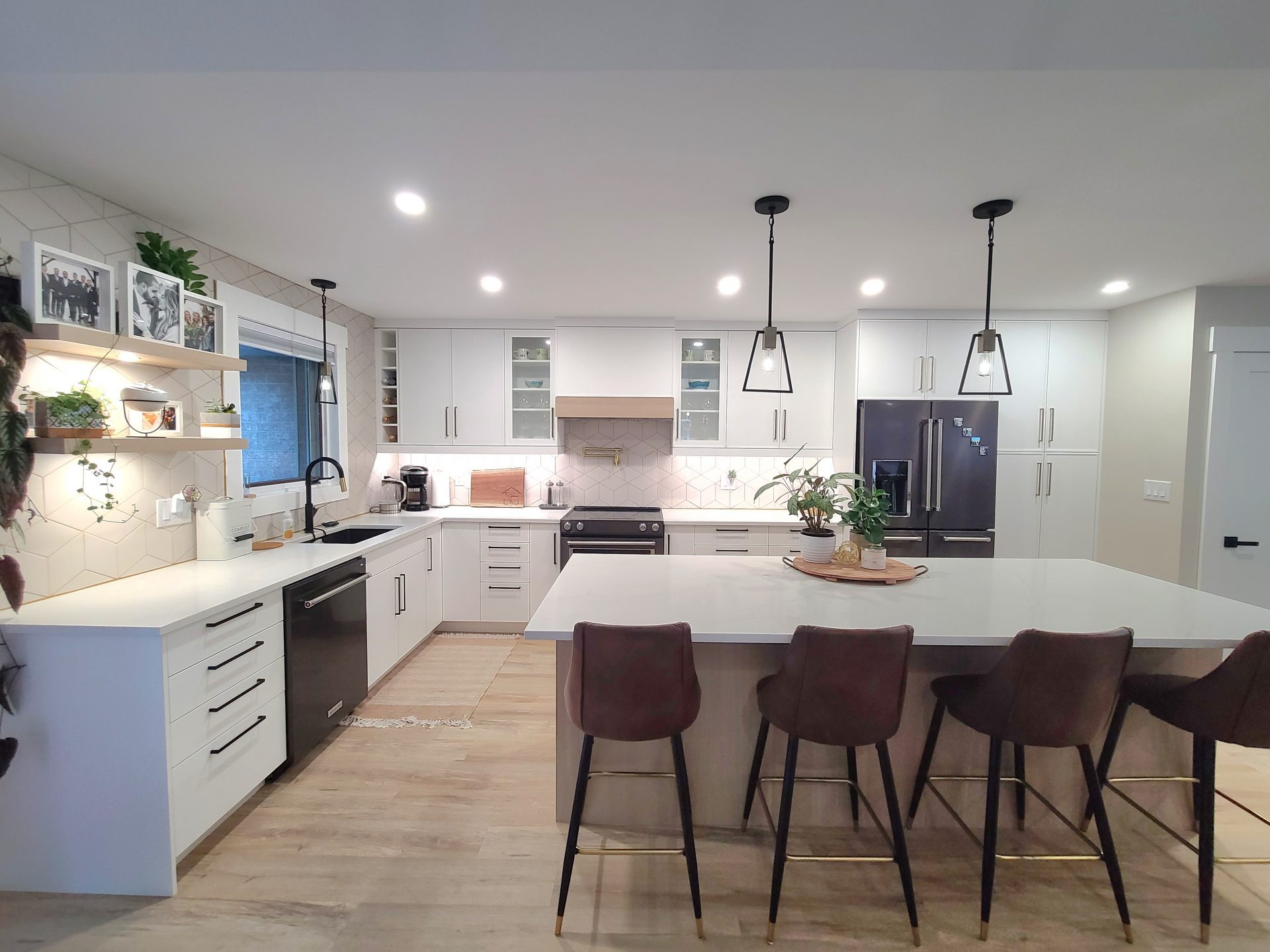 White kitchen with geometric tile backsplash, black cone pendant lights, dark fridge, and mauve velvet bar stools.