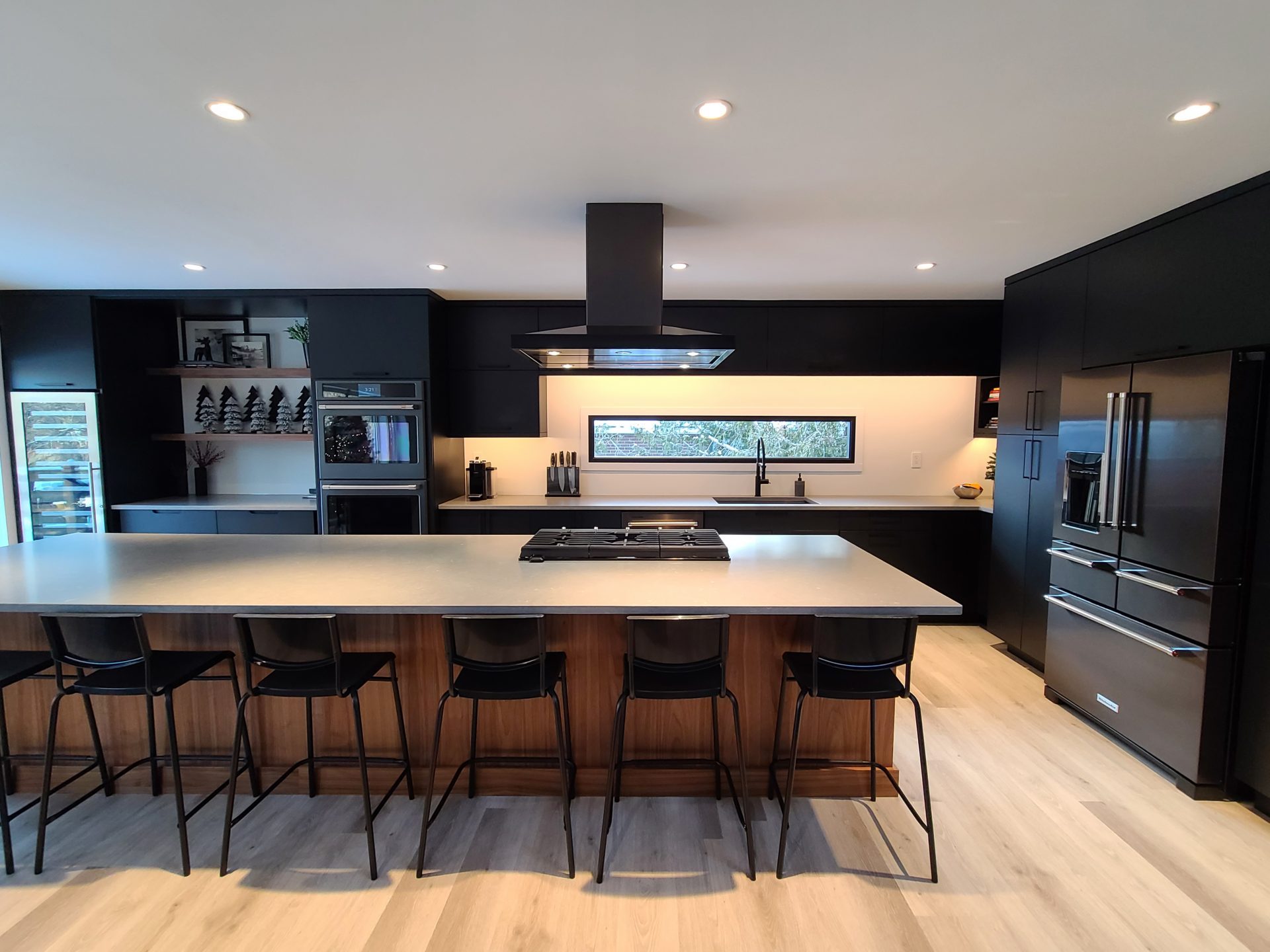 Sleek black kitchen with wood-front island, black hood, and stainless steel appliances.