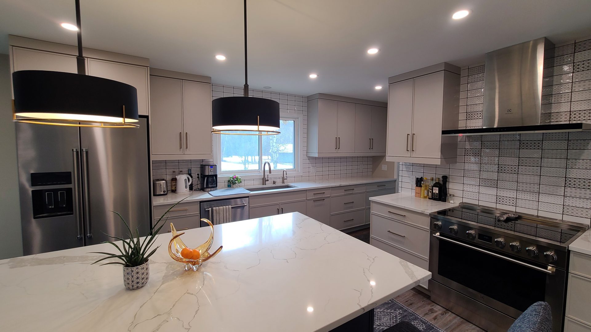 Light gray kitchen with patterned tile backsplash, black and gold pendant lights, and a marble-look island.