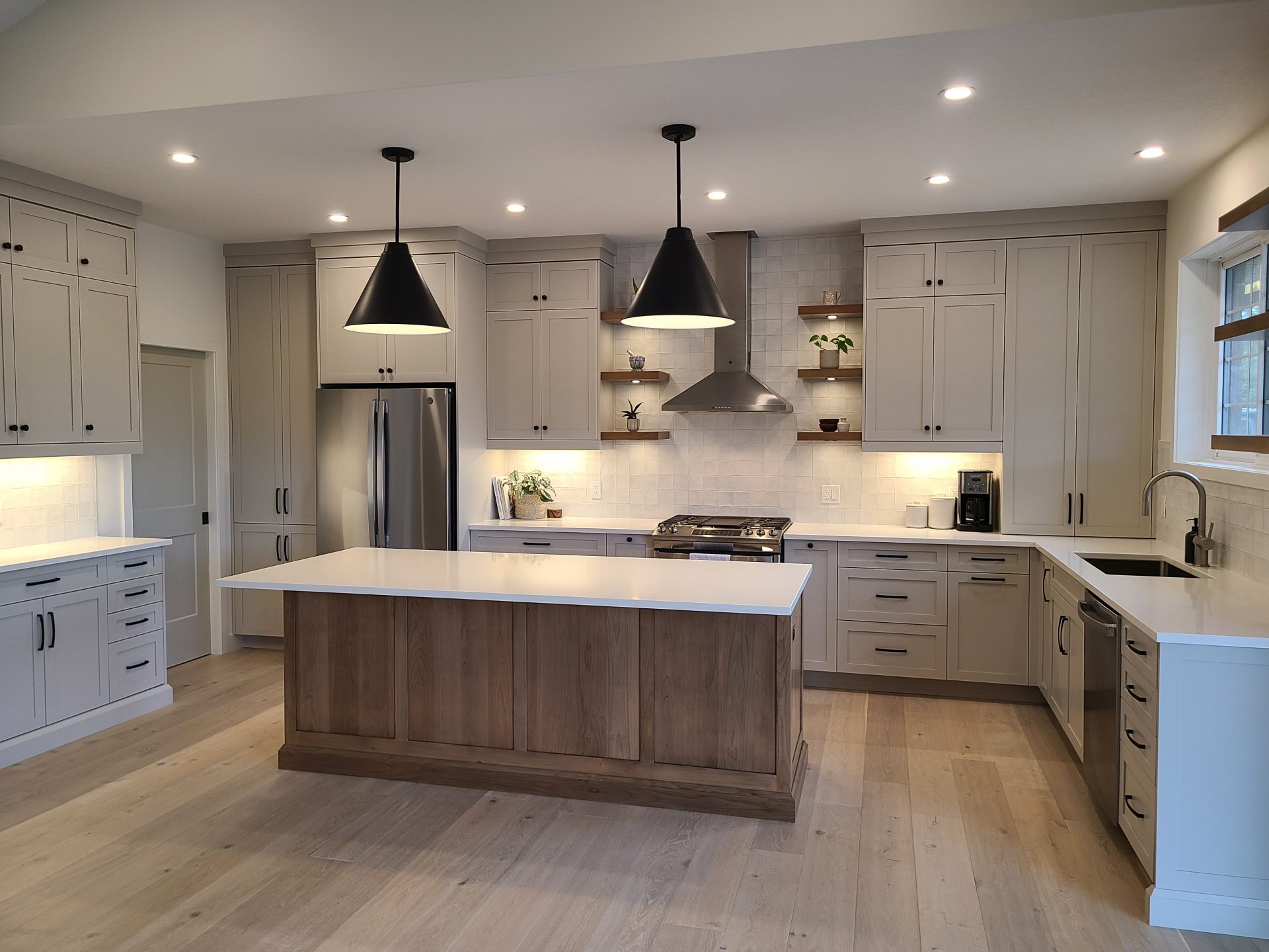 Light gray kitchen with a natural wood island, black pendant lights, and open wood shelving above the range.