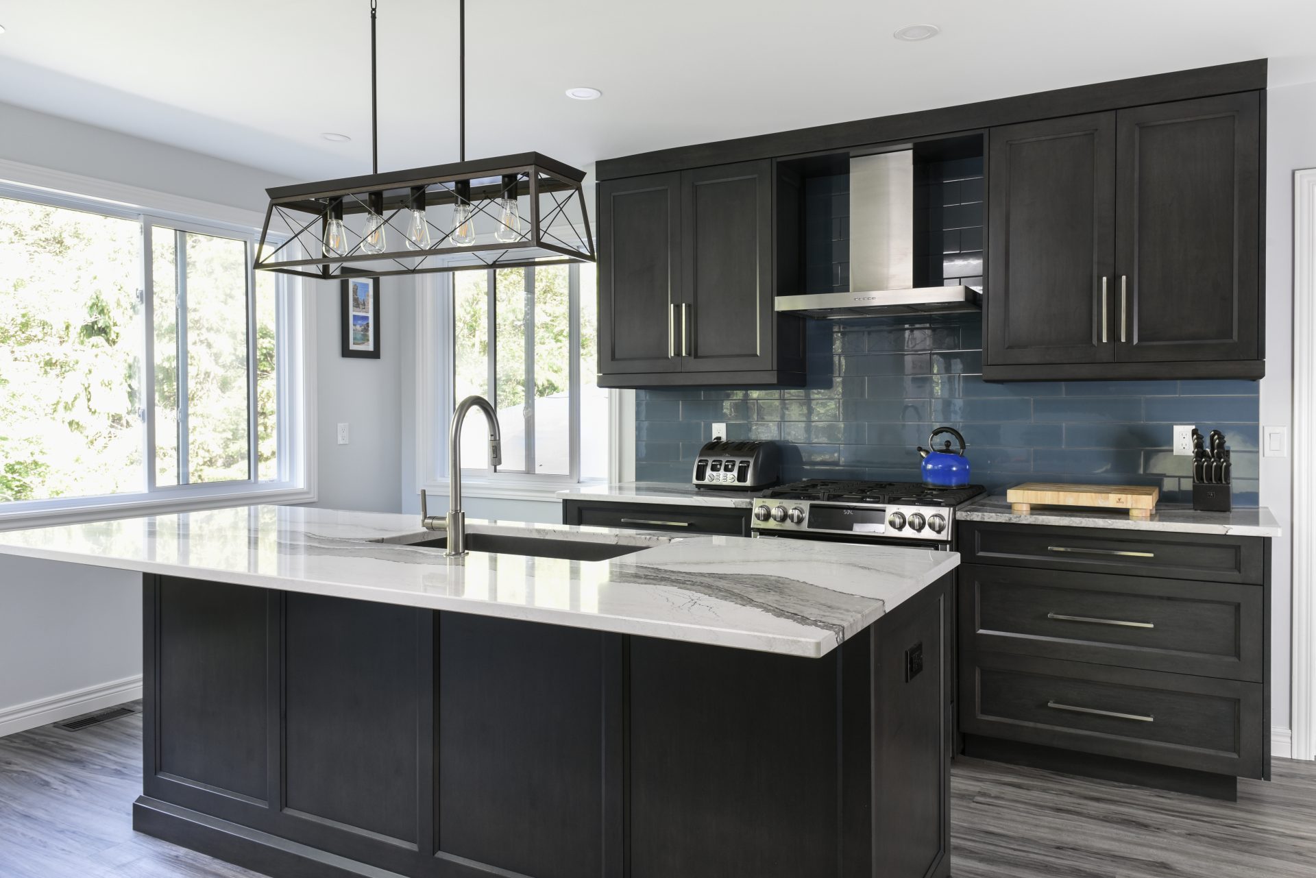 Dark charcoal kitchen with blue subway tile backsplash, white marble countertops, and an industrial-style island light fixture.